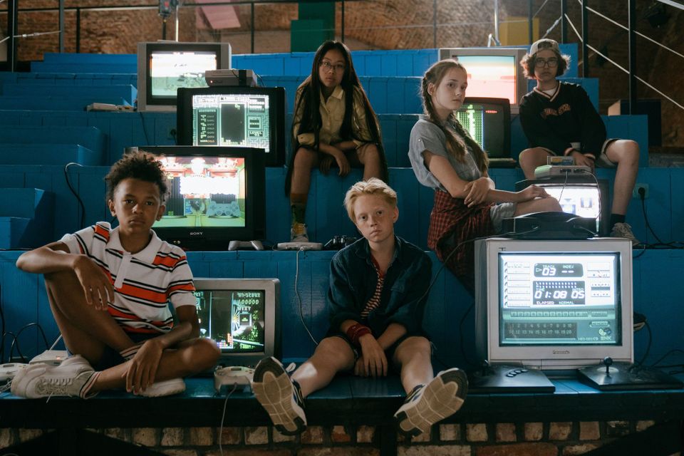 Bored kids surrounded by rad video game systems on CRT displays